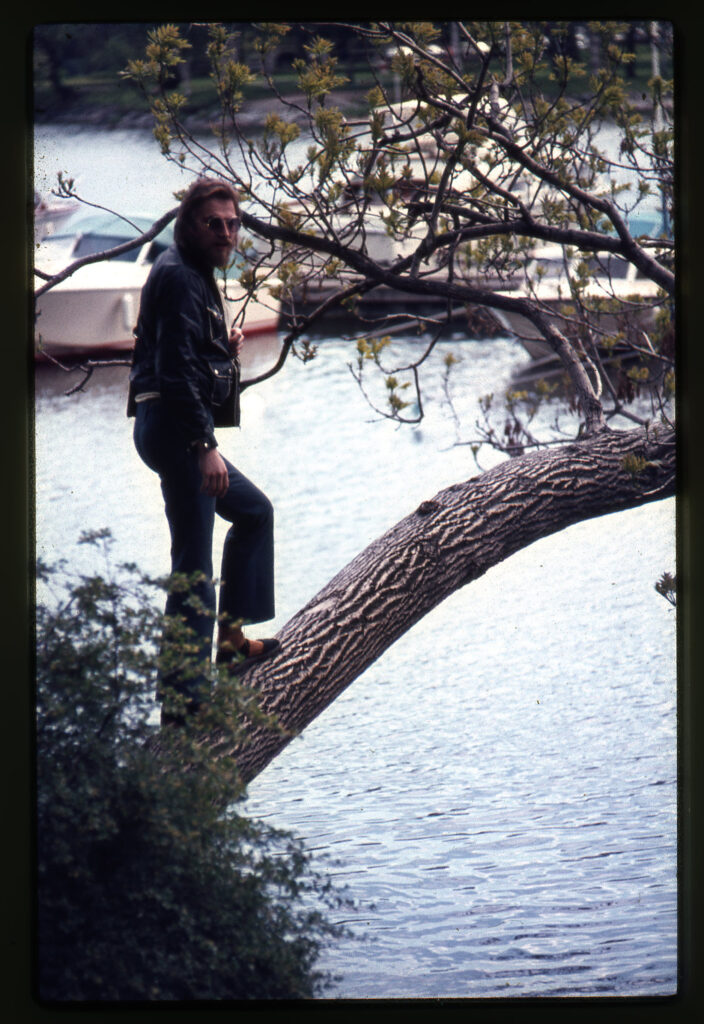 Man står på en lutande trädstam ovanför vatten med båtar.