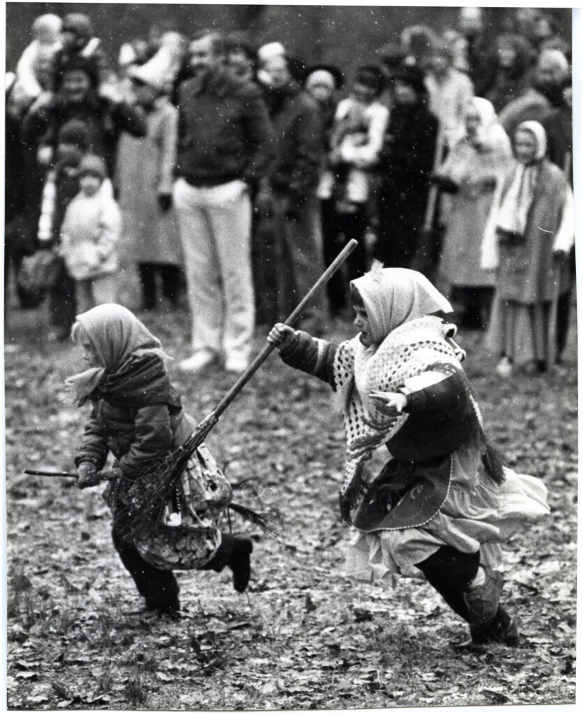 Två barn utklädda till påskkärringar springer med kvastar.