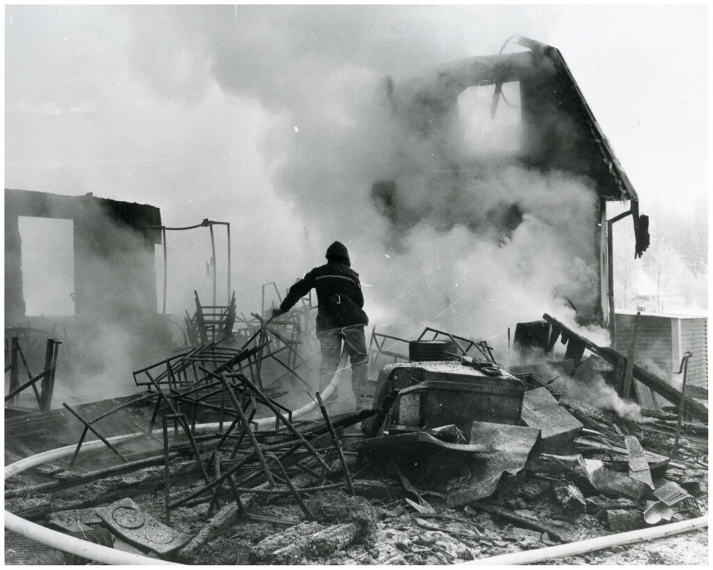 Brandman med vattenslang bland de rykande resterna efter en byggnad.