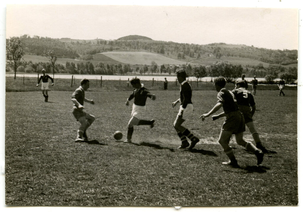 Fotbollsmatch, fem spelare och bollen i fokus.