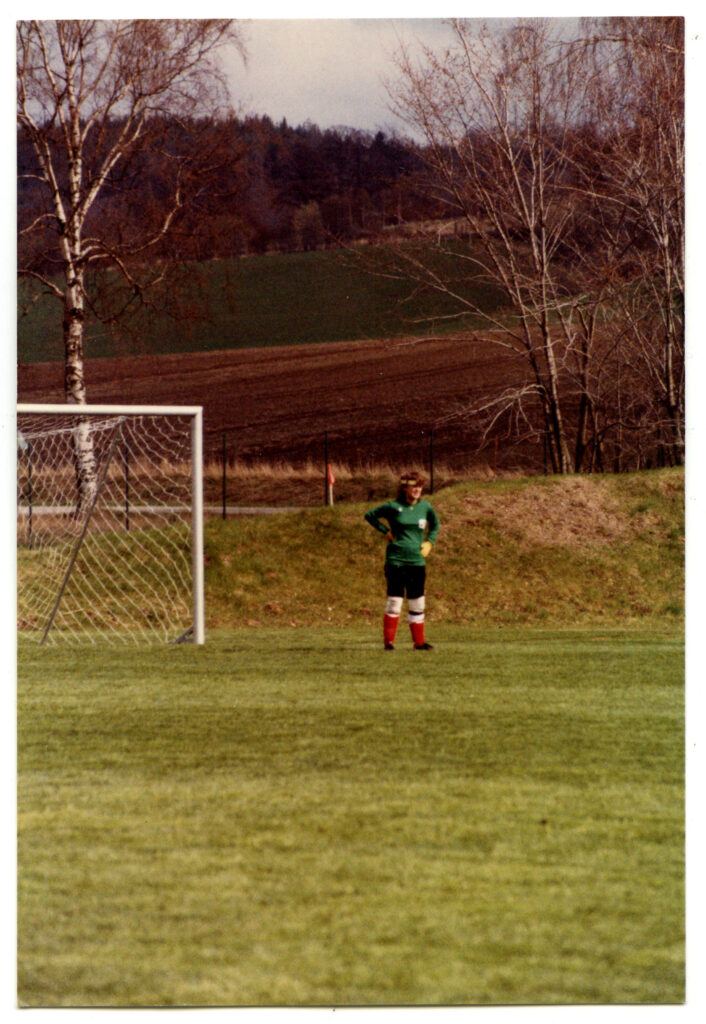 Kvinna i grön dräkt nära ett fotbollsmål.